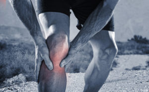52285034 - young sport man with strong athletic legs holding knee with his hands in pain after suffering muscle injury during a running workout training in trail desert dirt road in black and white